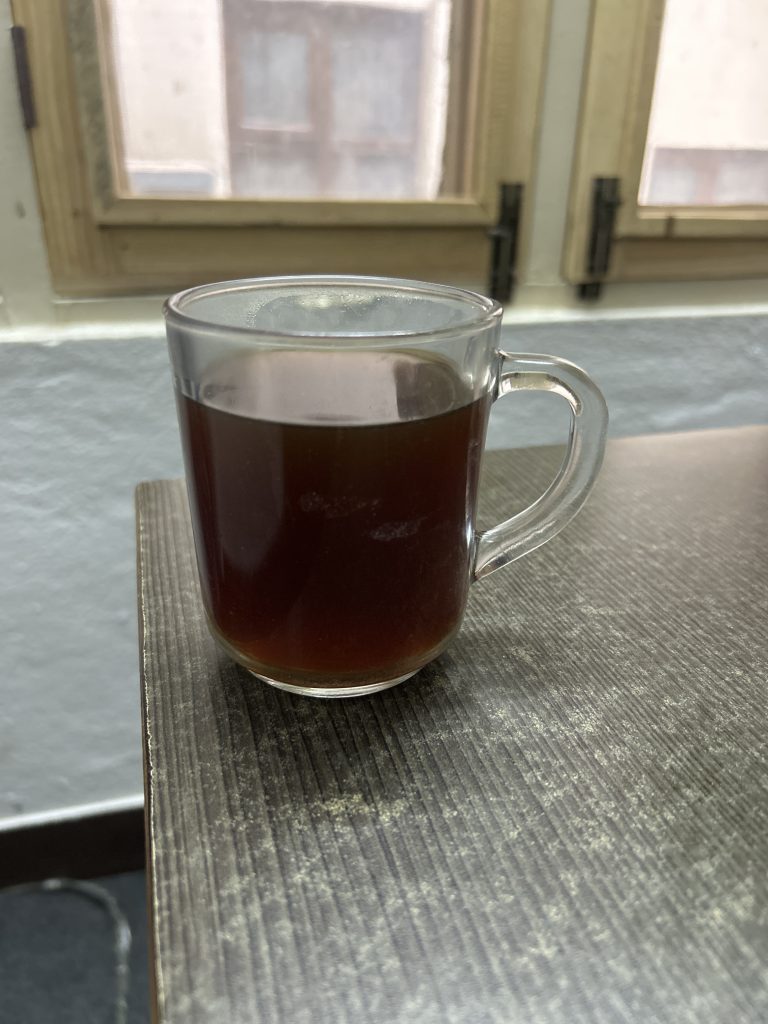 A clear glass mug filled with dark coffee sits on a wooden table near a window.