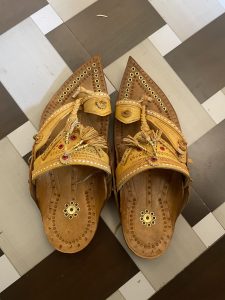 Traditional Indian leather sandals with intricate detailing and embellishments, placed on a checkered floor. It's called Kolhapuri Paytan