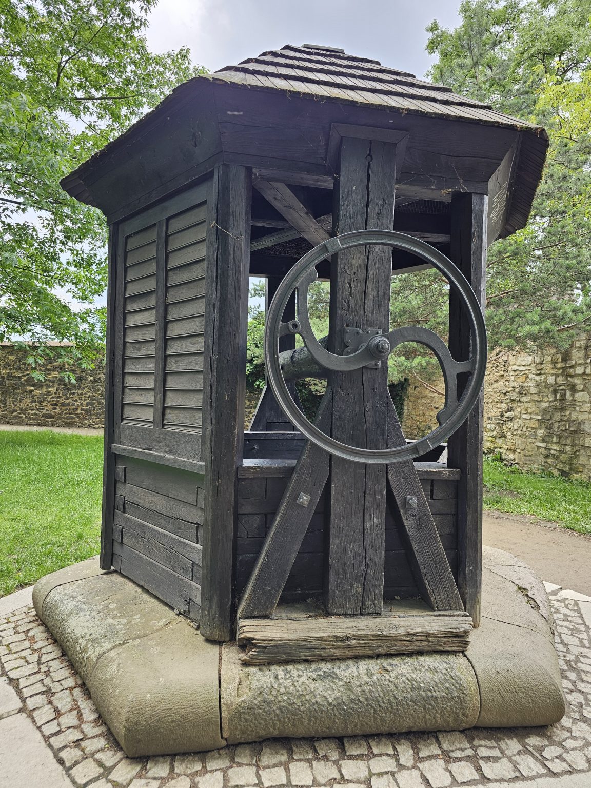 A traditional wooden well structure with a roof, a crank wheel, and a stone base, located in Vyšehrad, Prague.