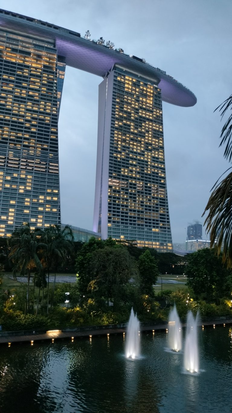 Marina Bay Sands, Singapore, captured at dusk with illuminated fountains in the foreground and lush greenery surrounding the iconic architectural marvel.