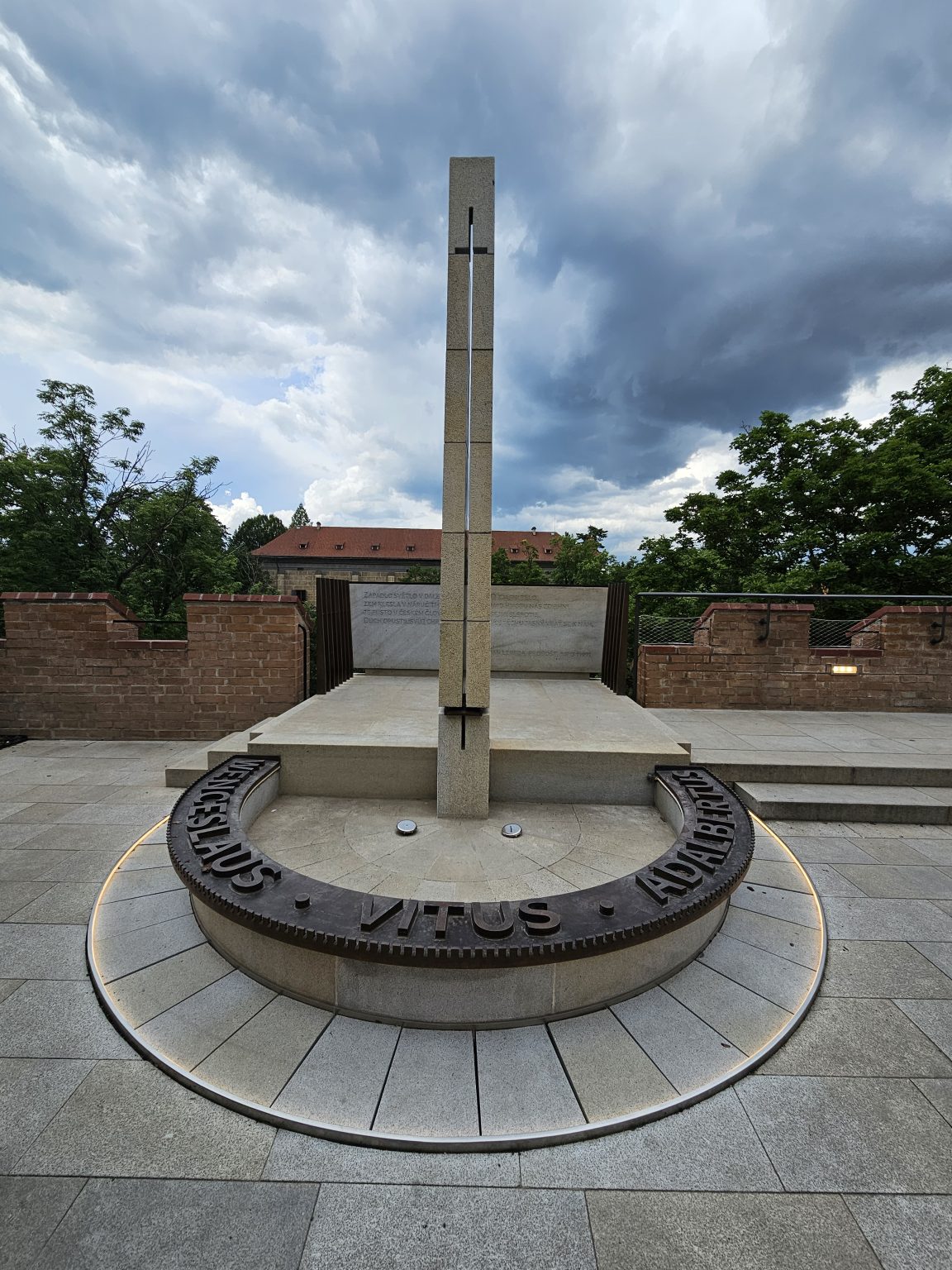 The New Provostry at Prague Castle. In the center, a tall stone cross stands set upon a circular base with the inscription "LAUS VITUS."