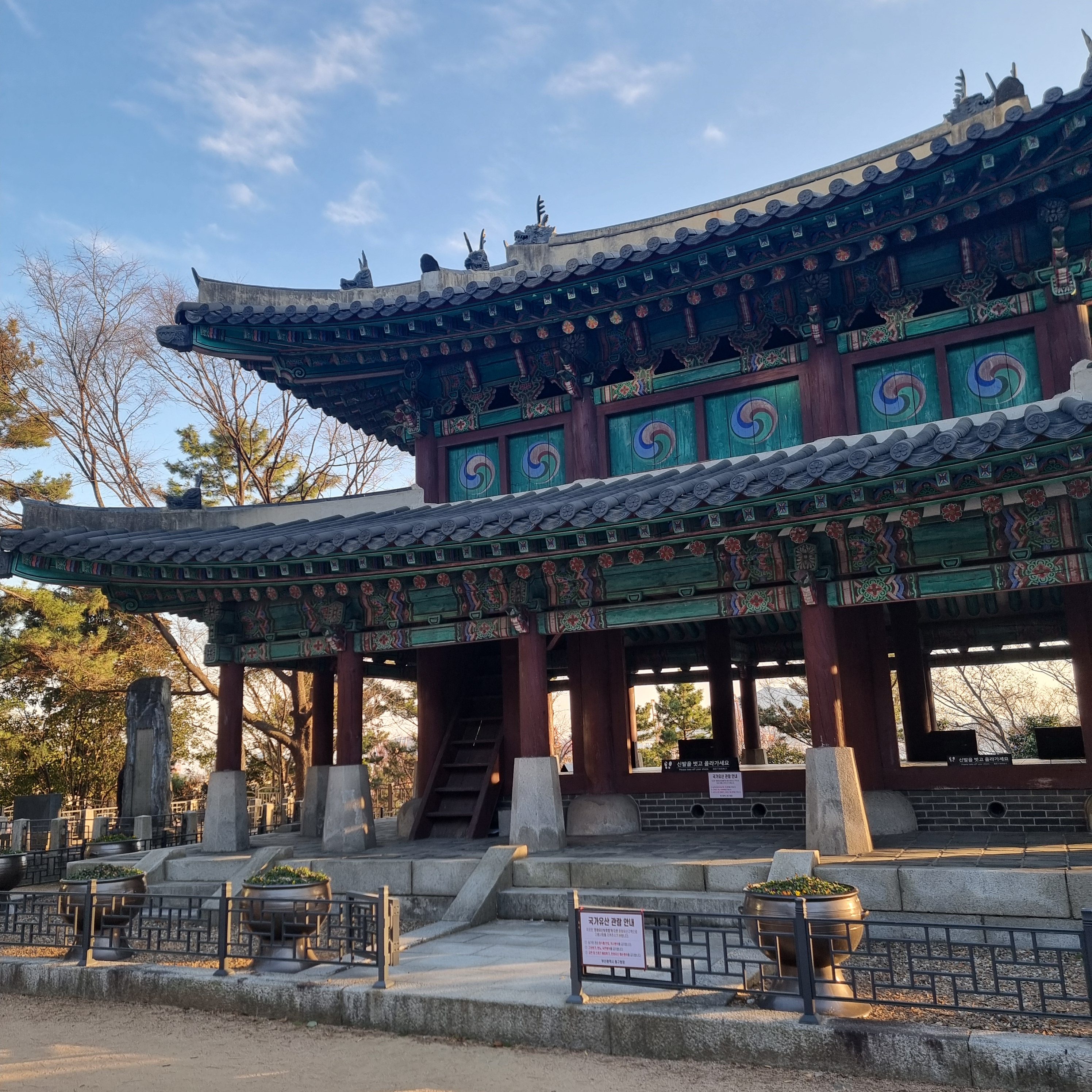 A traditional Korean busanjin pavilion with intricate wooden detailing and colorful painted designs, surrounded by trees on a clear day.