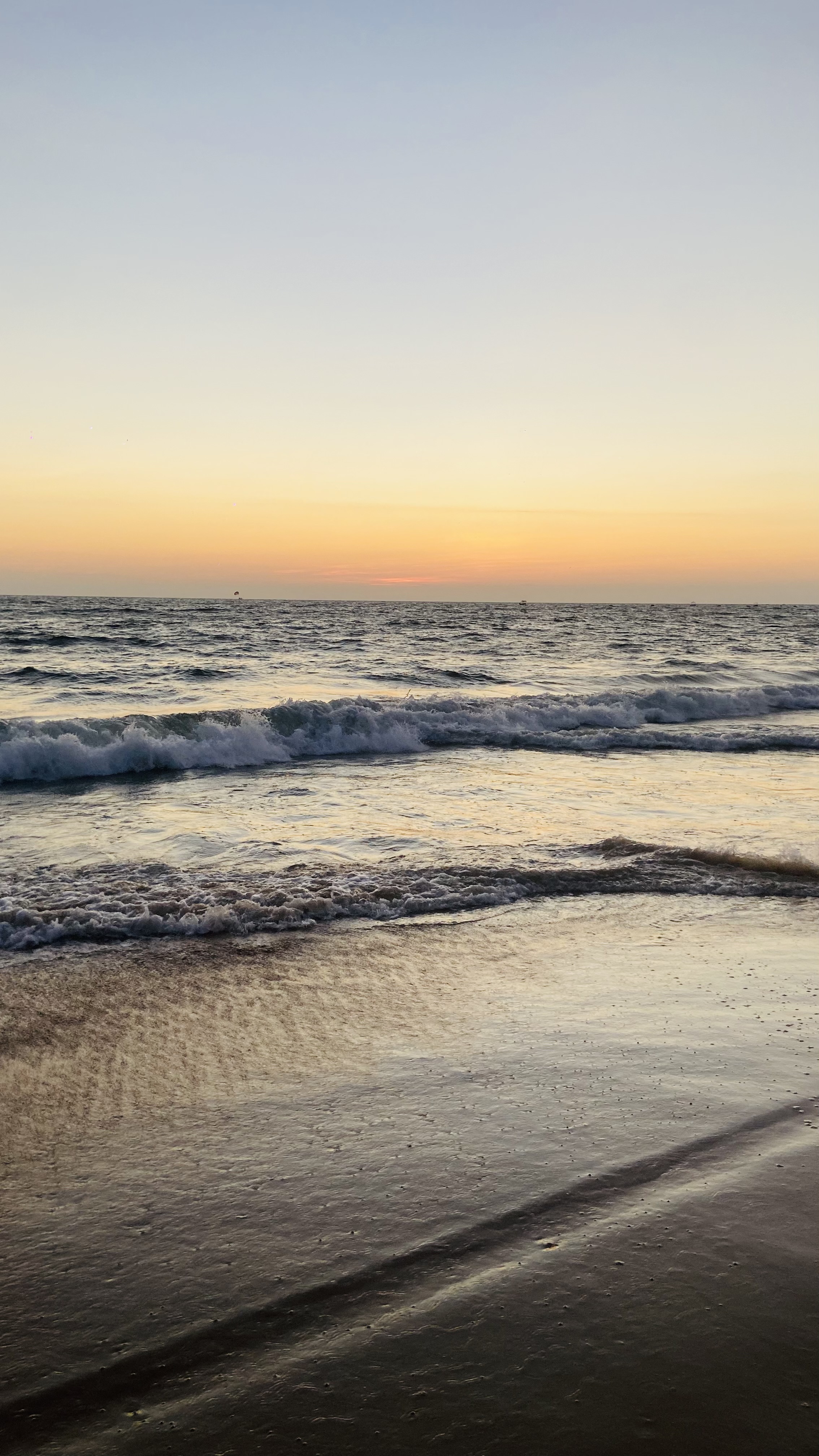 A serene beach at sunset with gentle waves rolling onto the shore, reflecting the warm hues of the sky in golden and orange tones.