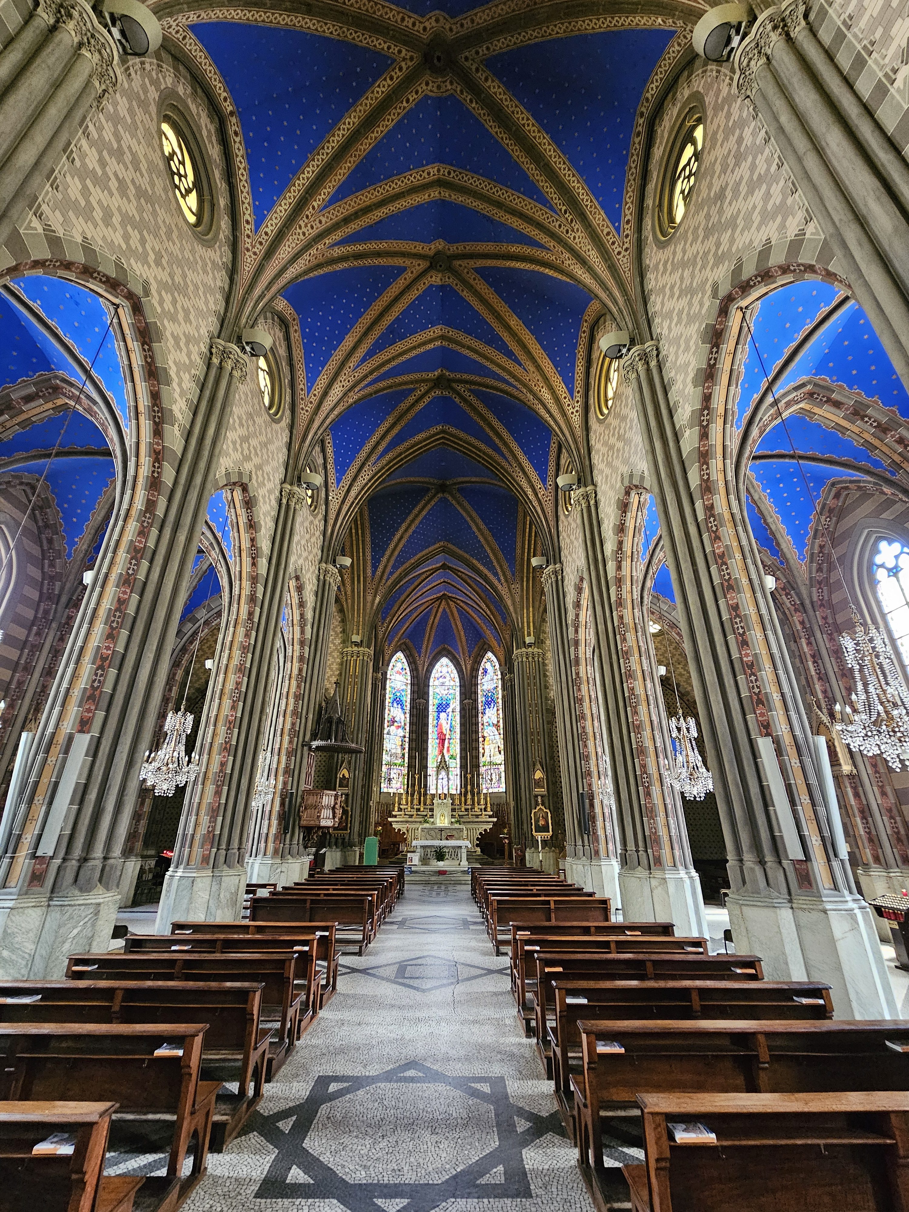 The interior of a church, santa maria sopra minerva or santa giulia in turin (torino), italy. The church features high, vaulted ceilings painted blue with gold stars, supported by tall, ornate columns. Rows of wooden pews line the central aisle, leading towards a brightly lit altar and stained glass windows.
