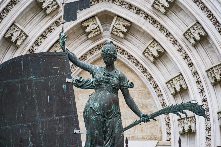 Replacement copy of Giraldillo, a bronze statue of a woman holding a flag and a palm branch in front of an ornate architectural stone archway, featuring intricate carvings and details.