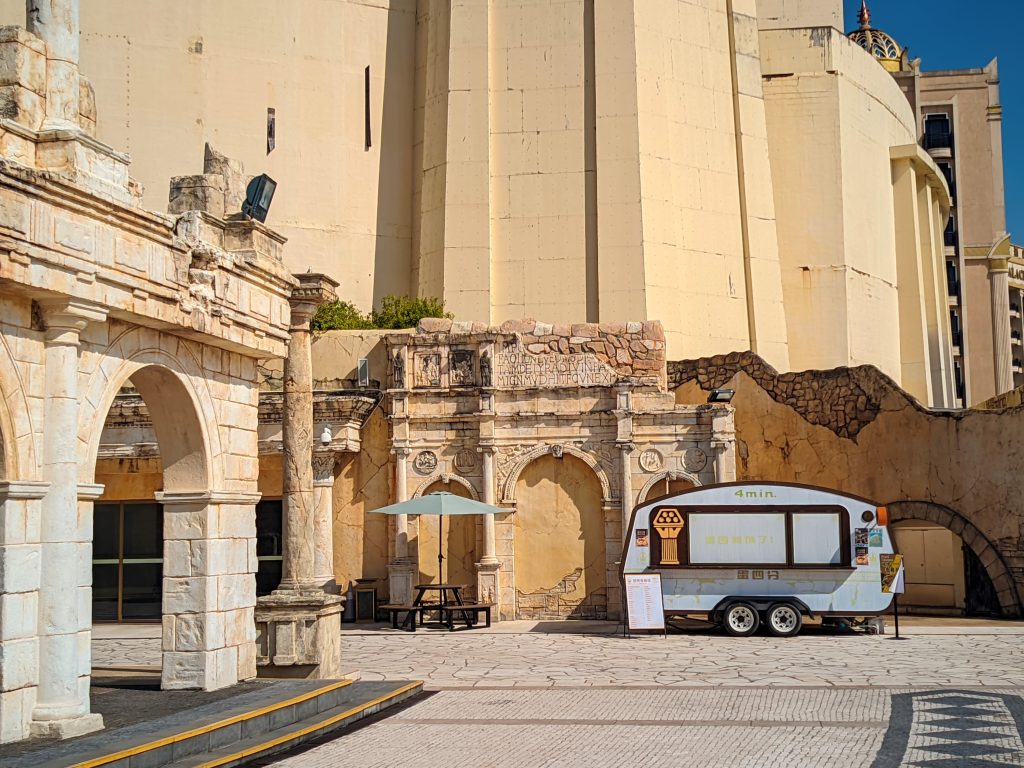 An Ice Cream truck parked between the Roman historical inspired or replica buildings.