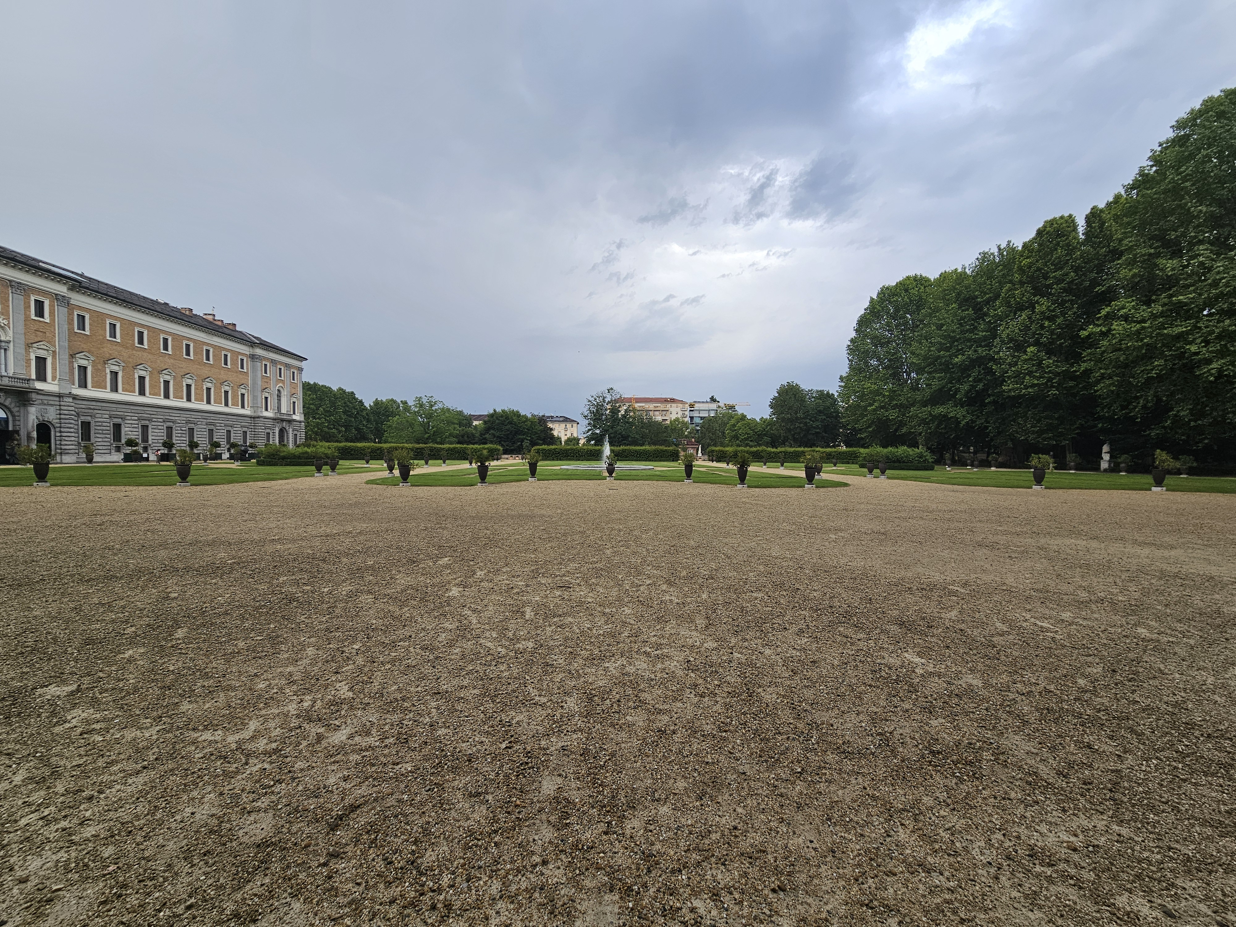 An evening view of the Royal Gardens (Giardini Reali) at the Royal Palace of Turin (Palazzo Reale di Torino). The garden is with a gravel courtyard, trimmed hedges, and the palace building visible in the background.