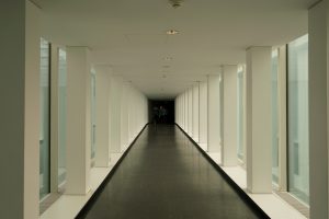 A long, modern corridor with large windows on both sides and two people walking in the distance.