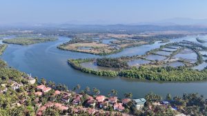 Sal River in Cavelossim, Goa, winding through lush green mangroves and small islands before meeting the Arabian Sea. The river is surrounded by traditional Goan houses with red-tiled roofs and palm trees.