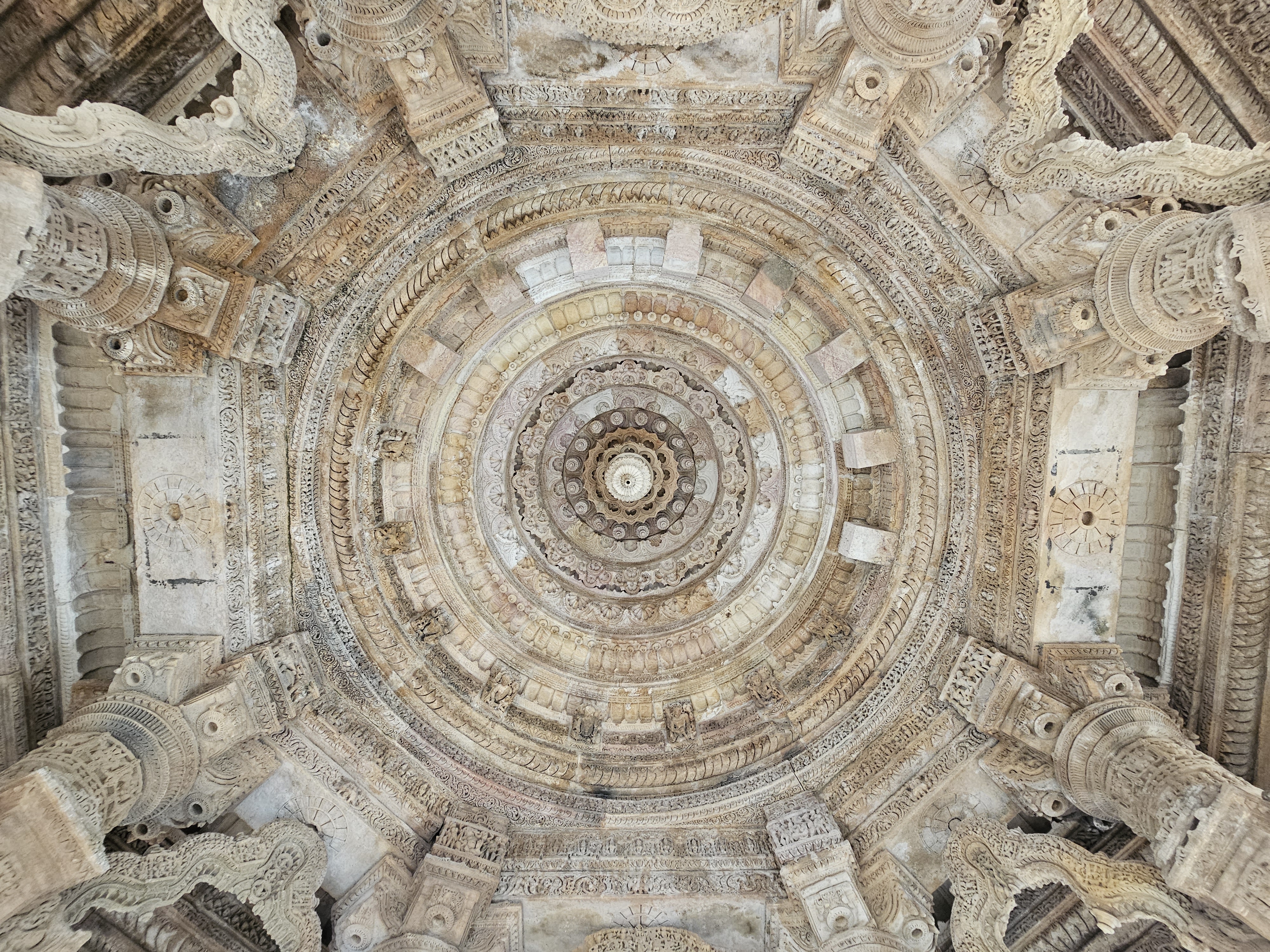 The elegantly carved ceiling of the Sun Temple in Modhera, Gujarat, India. The ceiling features concentric circles of detailed carvings and geometric patterns, radiating from a central point, and is supported by elaborately sculpted pillars.