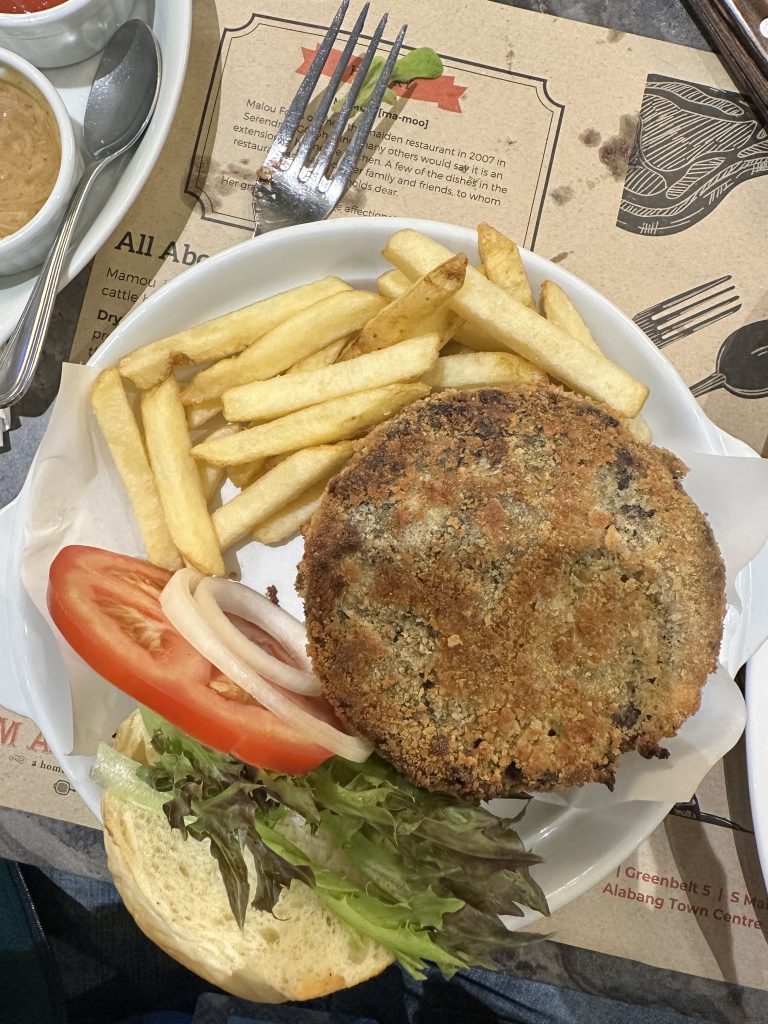 A plate with a burger, salad, and french fries. It is served on the table in a restaurant of Manila.