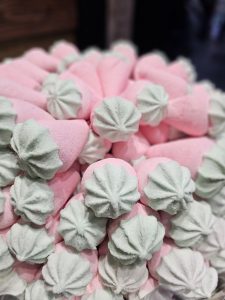 A close-up of a pile of pink and green meringue candies. The candies are cone-shaped with a swirled, star-shaped top. The pink part of the candy forms the base, while the green meringue is on top.