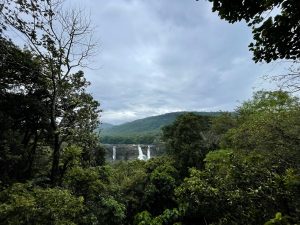 A very long view of Athirappilly Waterfalls in Kerala, India. Set against a backdrop of lush greenery and cloudy sky.