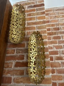 Two decorative metal wall sconces with a floral pattern, mounted on a rustic brick wall.