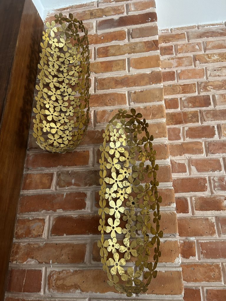 Two decorative metal wall sconces with a floral pattern, mounted on a rustic brick wall.