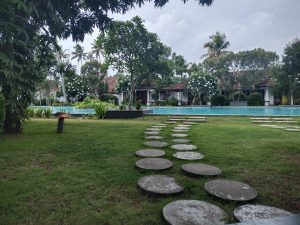 A serene landscape featuring a grassy lawn with a circular stone pathway leading to a swimming pool. 