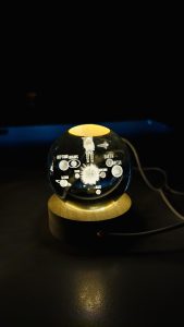 A glowing crystal ball on a wooden base features a 3D-engraved astronaut floating in space, surrounded by labeled planets such as Earth, Jupiter, Mars, and others.
