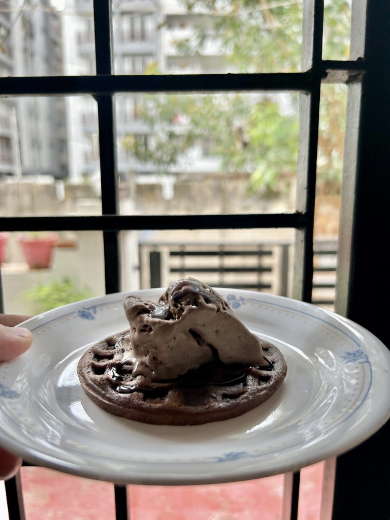 A delicious waffel dessert topped with creamy sauce, nuts, chocolate chips, and crushed biscuits.