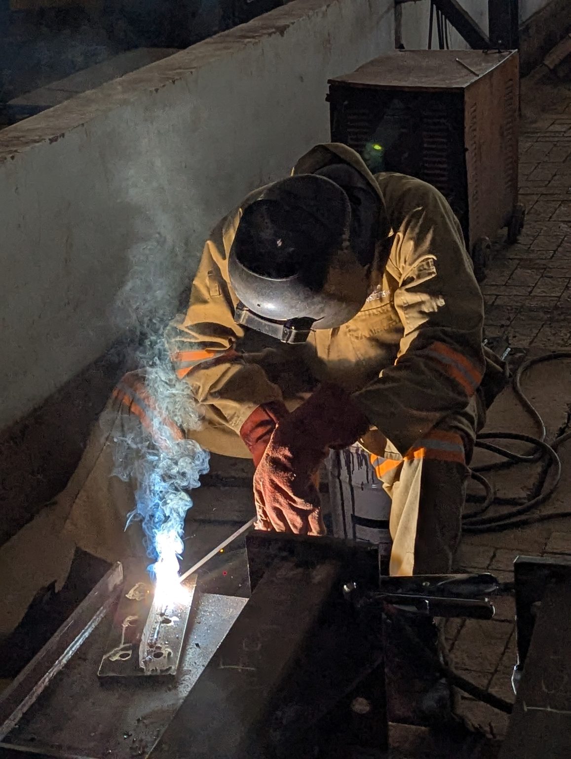 Close of a factory worker welding a heavy machine hinge