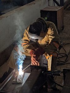 Close of a factory worker welding a heavy machine hinge