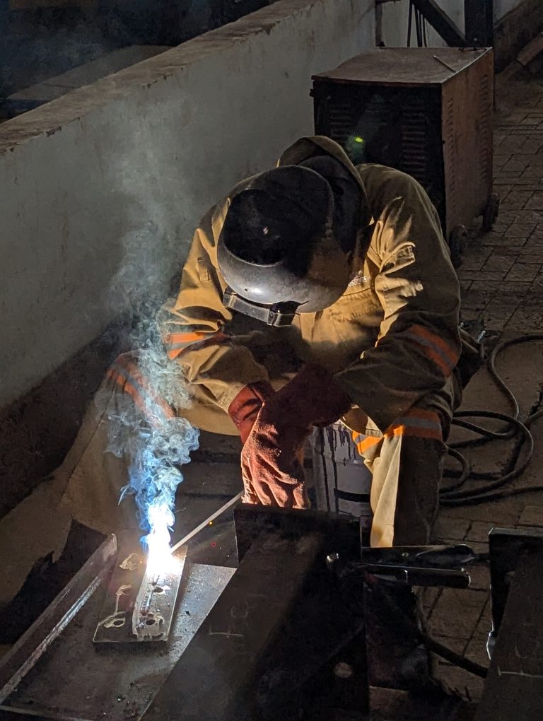 Close of a factory worker welding a heavy machine hinge