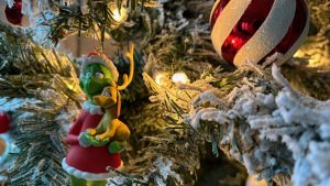 Closeup of a Christmas tree ornament of The Grinch and his dog, nestled in tree branches. Nearby is a red and white bauble ornament.