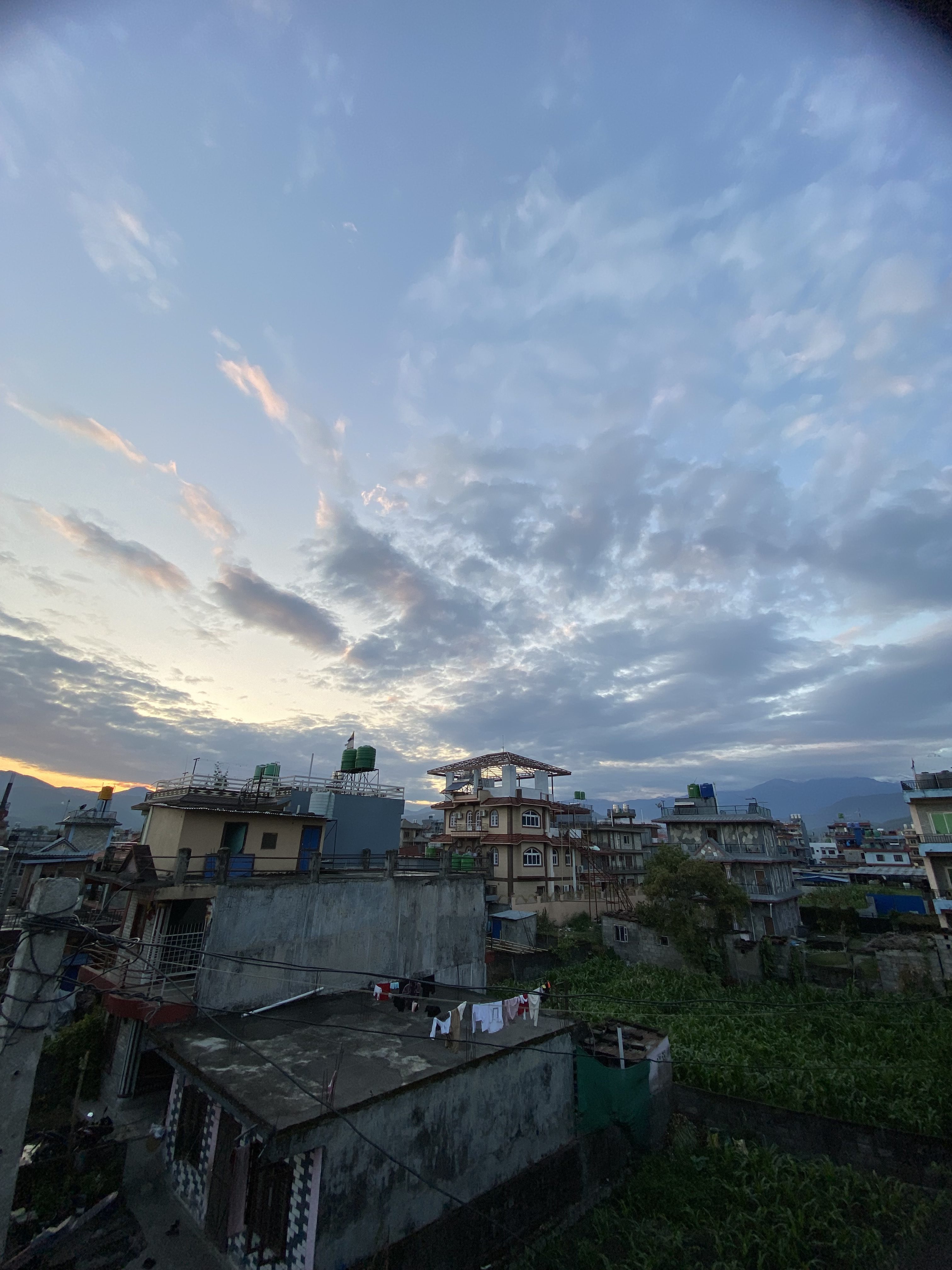 A panoramic view of a cityscape at dusk, featuring a series of buildings with varied architecture, some with exposed concrete and others with balconies