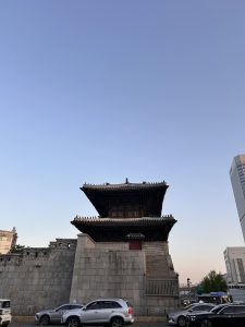 A traditional Asian pagoda-style structure stands prominently over a stone wall, with a clear sky in the background.
