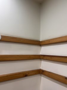 A corner of a room featuring three parallel wooden railings on each wall, set against light-colored walls.