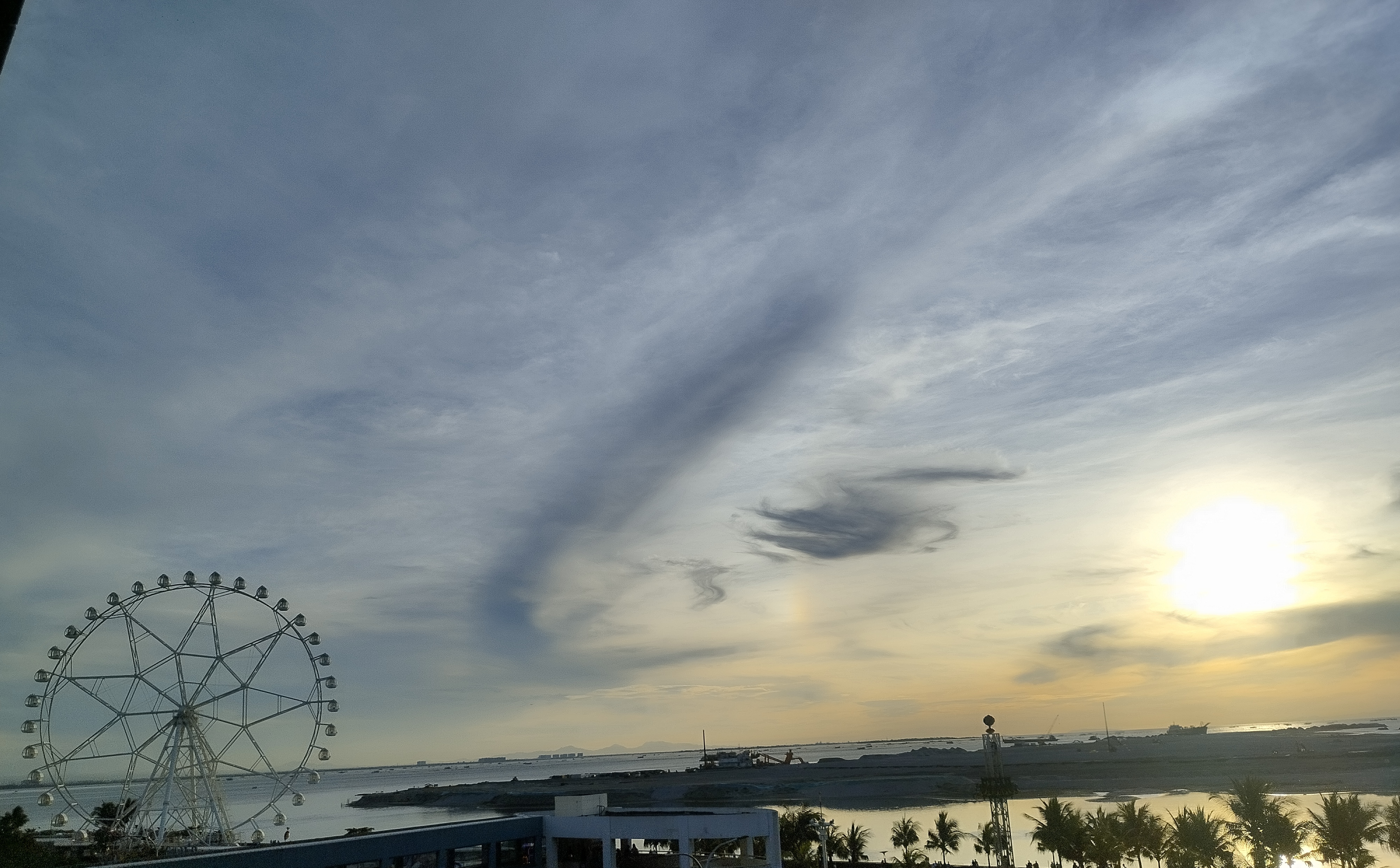 A scenic view of a large Ferris wheel by the waterfront during sunset.