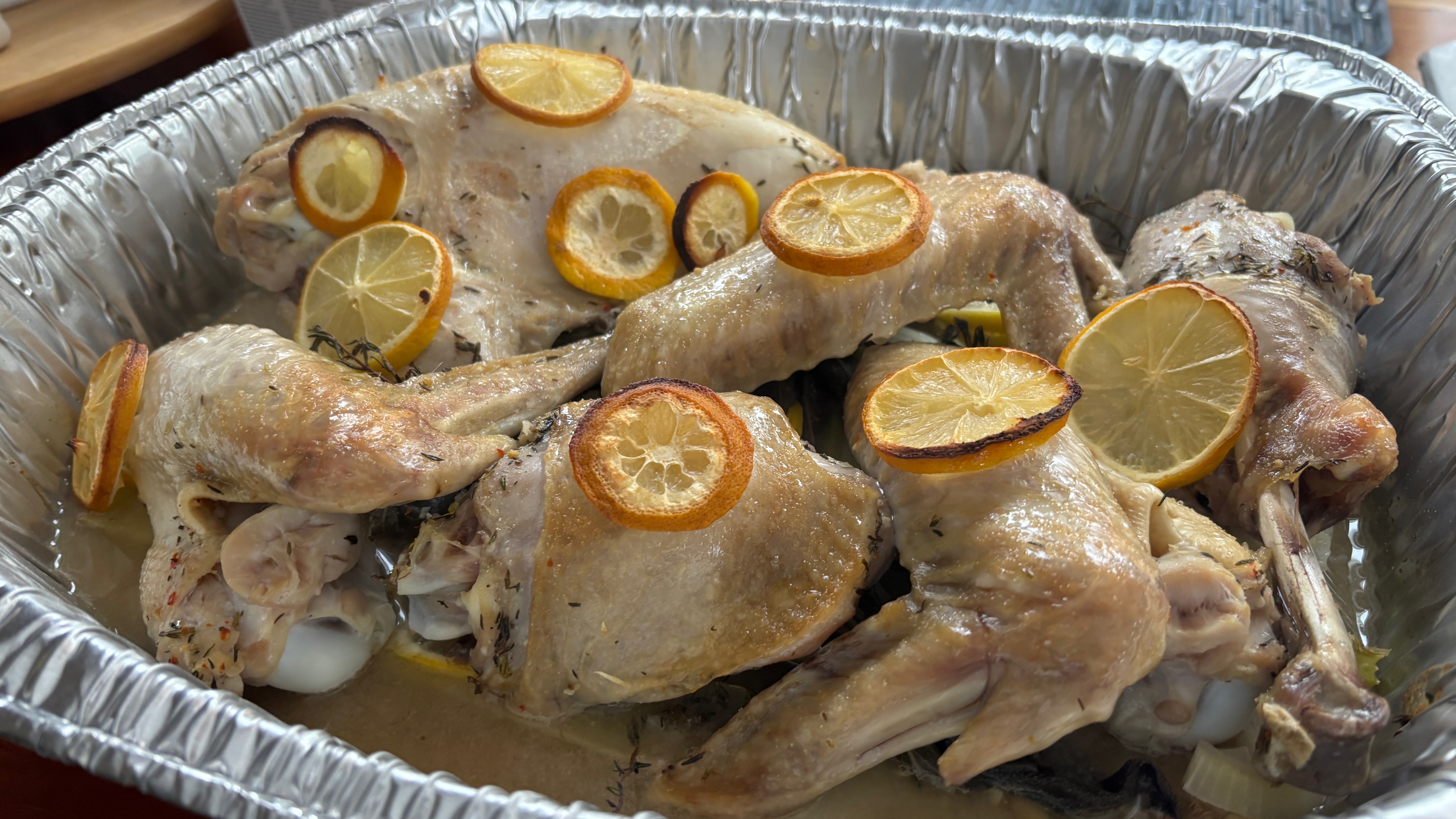 A cooked turkey, separated into parts. with lemon slices on top, sitting in an aluminum pan.