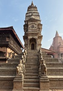 An ancient stone temple with intricate carvings and statues, featuring a steep stairway flanked by sculptures of figures and animals at Bhaktapur Durbar Square.