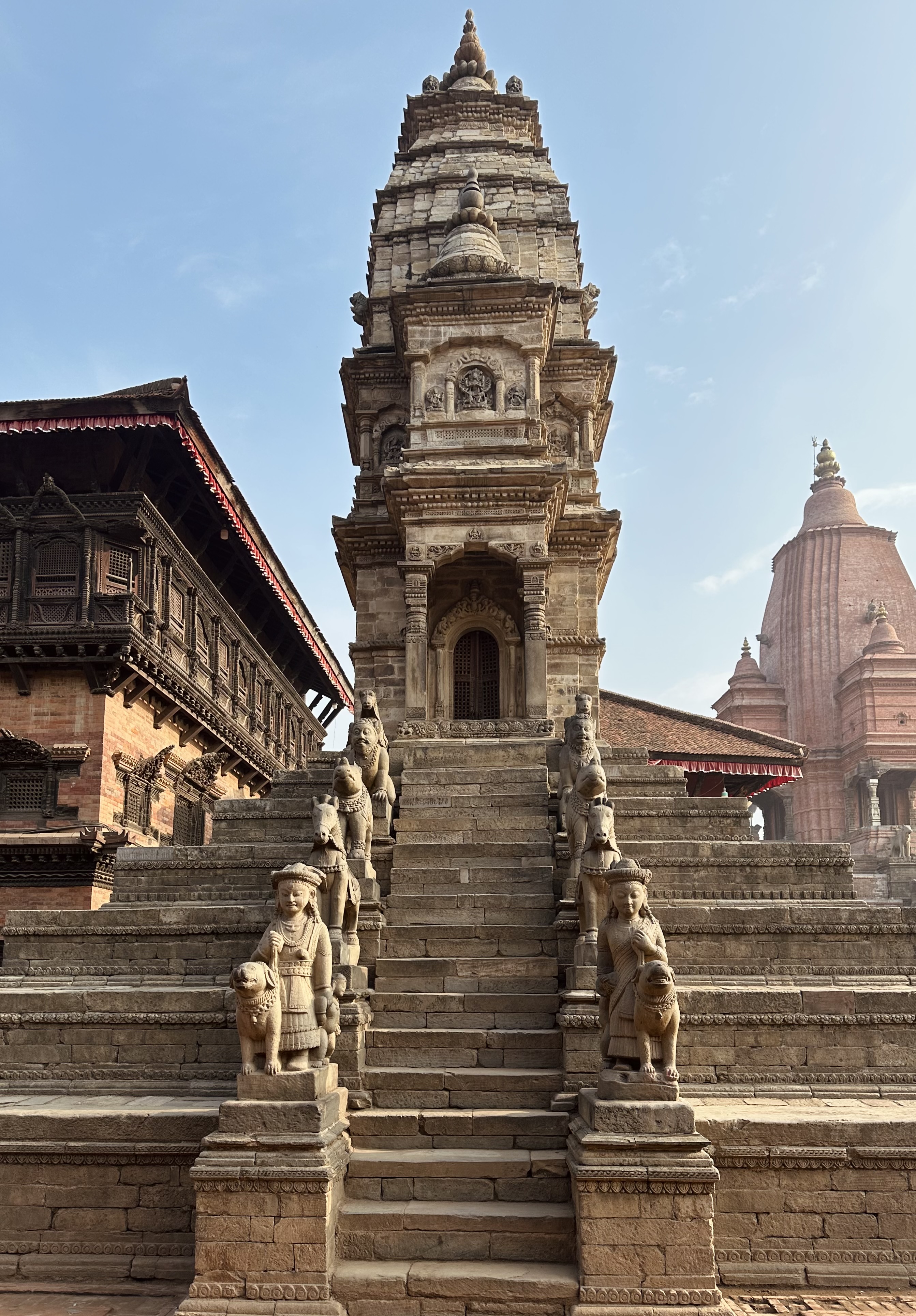 An ancient stone temple with intricate carvings and statues, featuring a steep stairway flanked by sculptures of figures and animals at Bhaktapur Durbar Square.