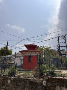 A small red temple with a traditional roof stands behind a wire fence. 