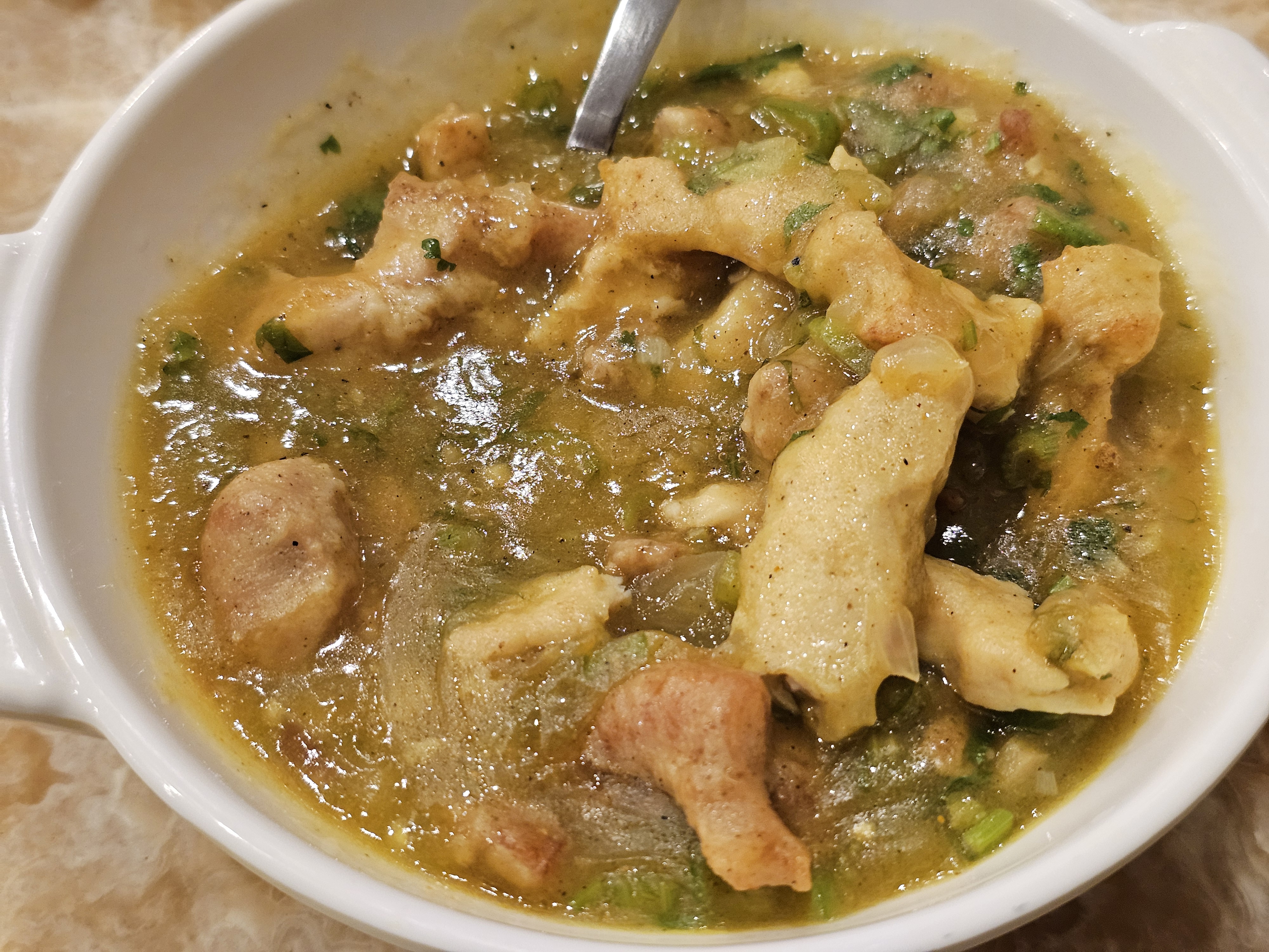 A bowl of ginger chicken curry, with tender pieces of chicken and ginger in a thick, savory broth. The curry has a greenish-brown color and is garnished with fresh herbs. Captured at a restaurant in Kozhikode, Kerala.