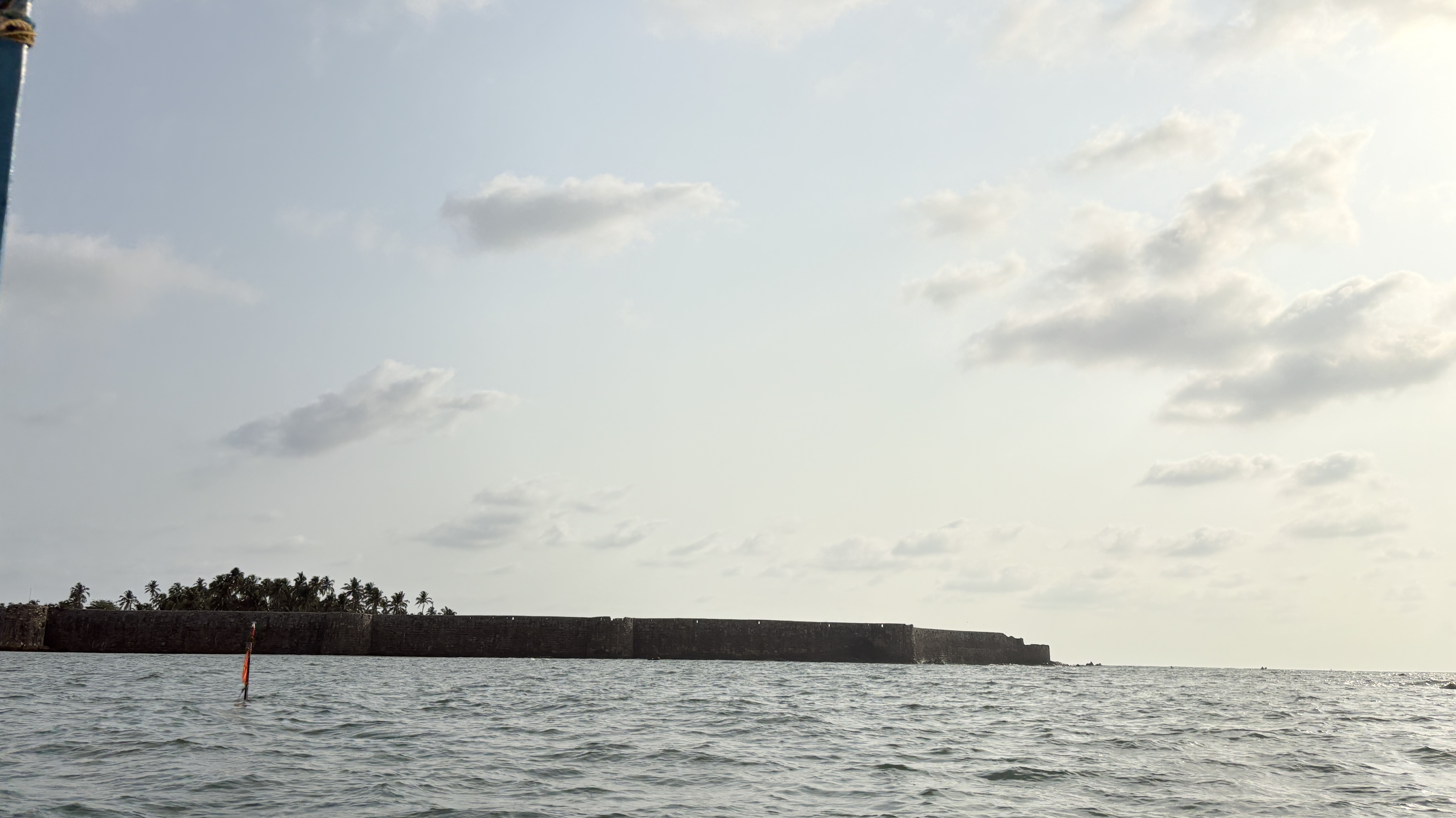 A distant view of a stone fortification along the shoreline, surrounded by calm waters.