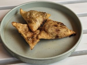 Three golden-brown, triangular chicken samosas were arranged on a light gray plate. The samosas appear to be freshly fried, with slightly crispy edges and a savory filling visible through the thin pastry. Captured from a restaurant in Kozhikode, Kerala.
