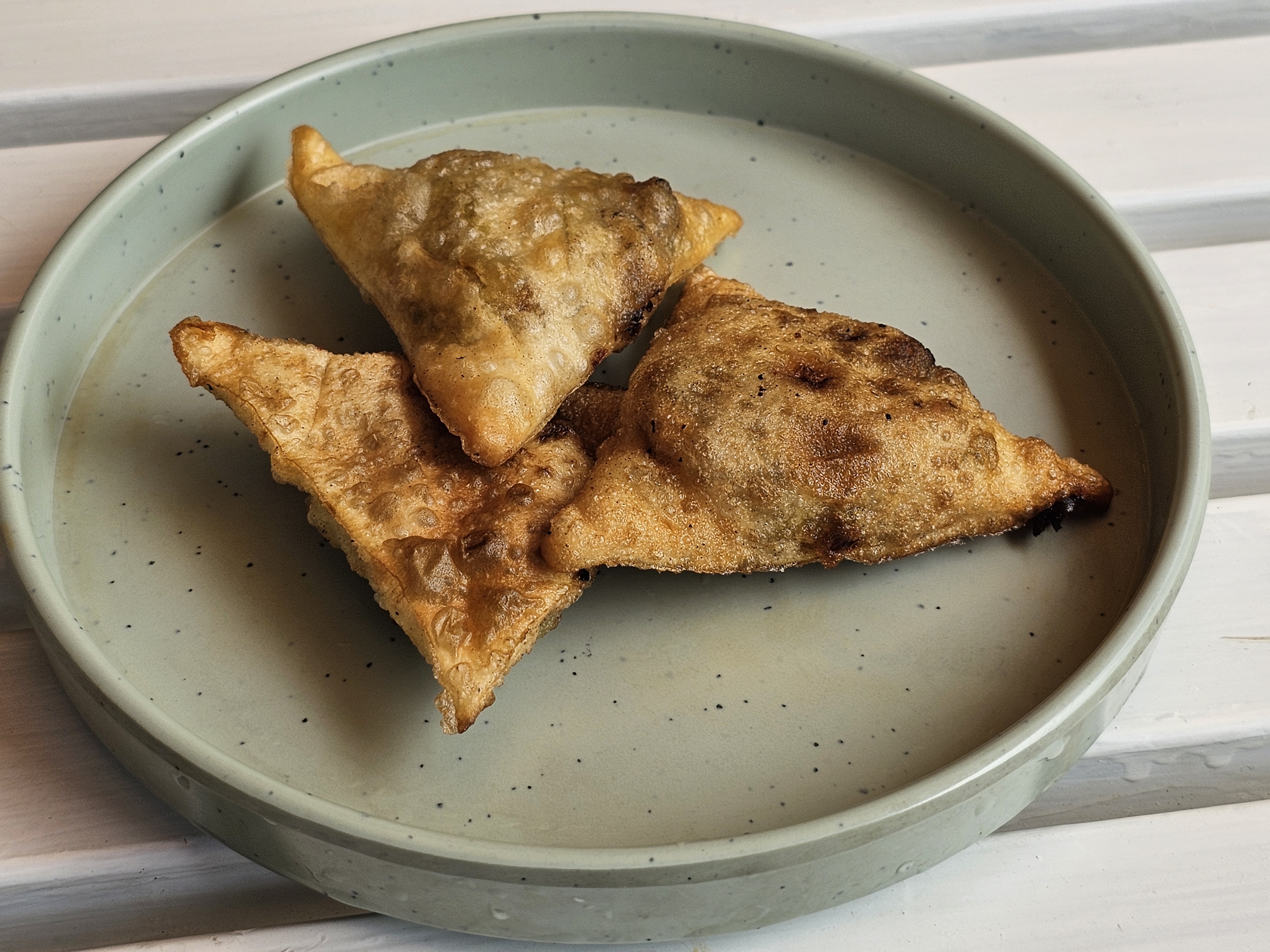 Three golden-brown, triangular chicken samosas were arranged on a light gray plate. The samosas appear to be freshly fried, with slightly crispy edges and a savory filling visible through the thin pastry. Captured from a restaurant in Kozhikode, Kerala.