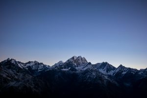 A panoramic view of a mountain range with snow-capped peaks under a clear blue sky at twilight.