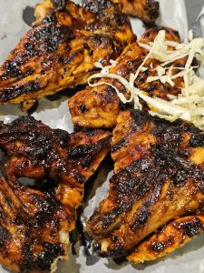 A close-up of grilled chicken (Al Faham barbecued) pieces, with a slightly charred and seasoned appearance, arranged on a light-colored surface, possibly a serving plate. Shredded cabbage or lettuce is lightly scattered on the side. It was captured in Kozhikode, Kerala.