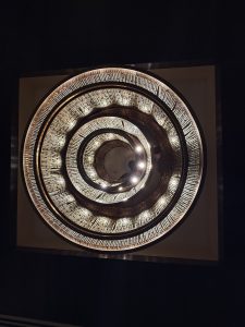 A ceiling with concentric circles of illuminated tiles creating a spiral pattern, embedded with small lights, set against a dark background.