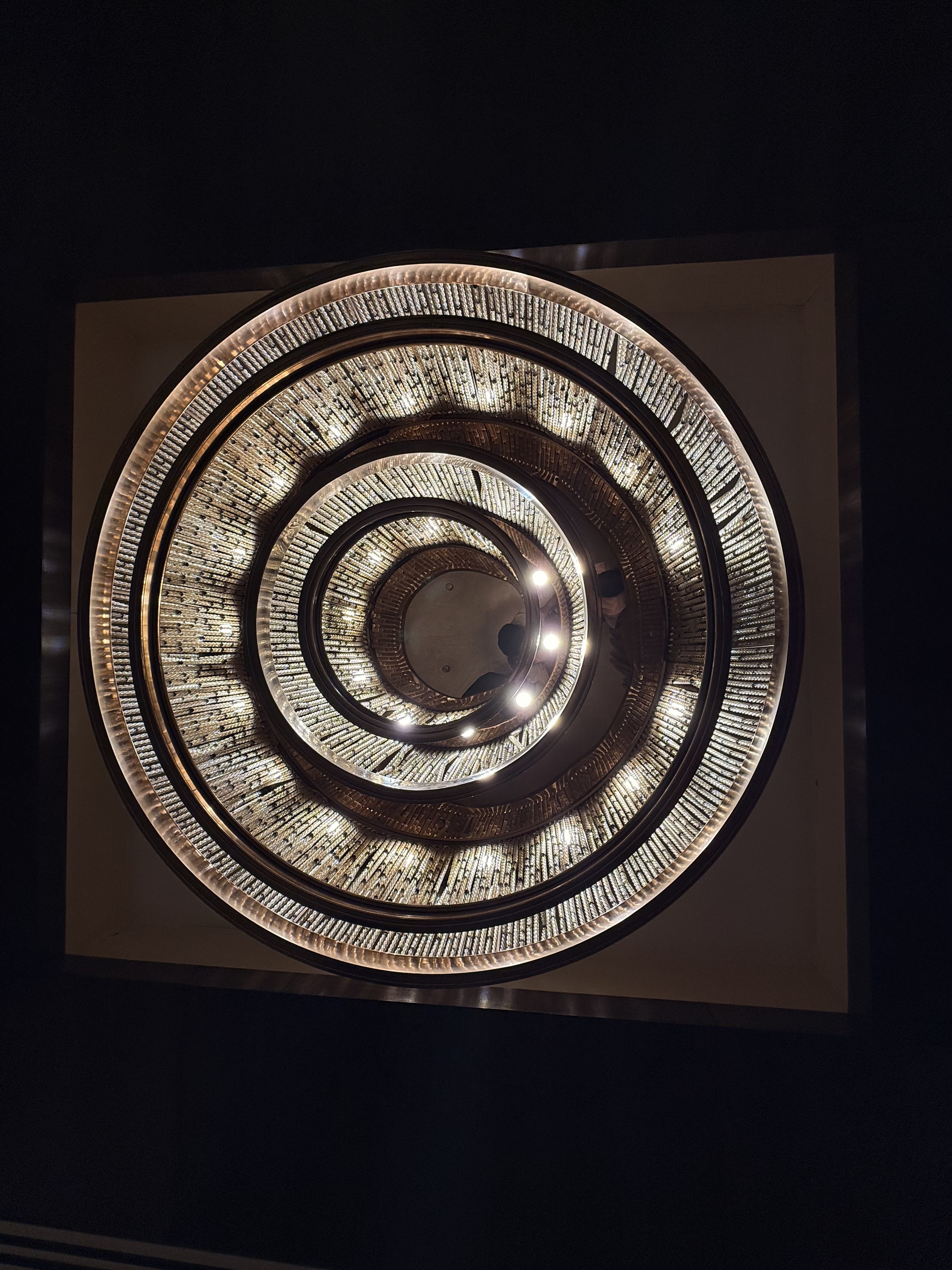 A ceiling with concentric circles of illuminated tiles creating a spiral pattern, embedded with small lights, set against a dark background.