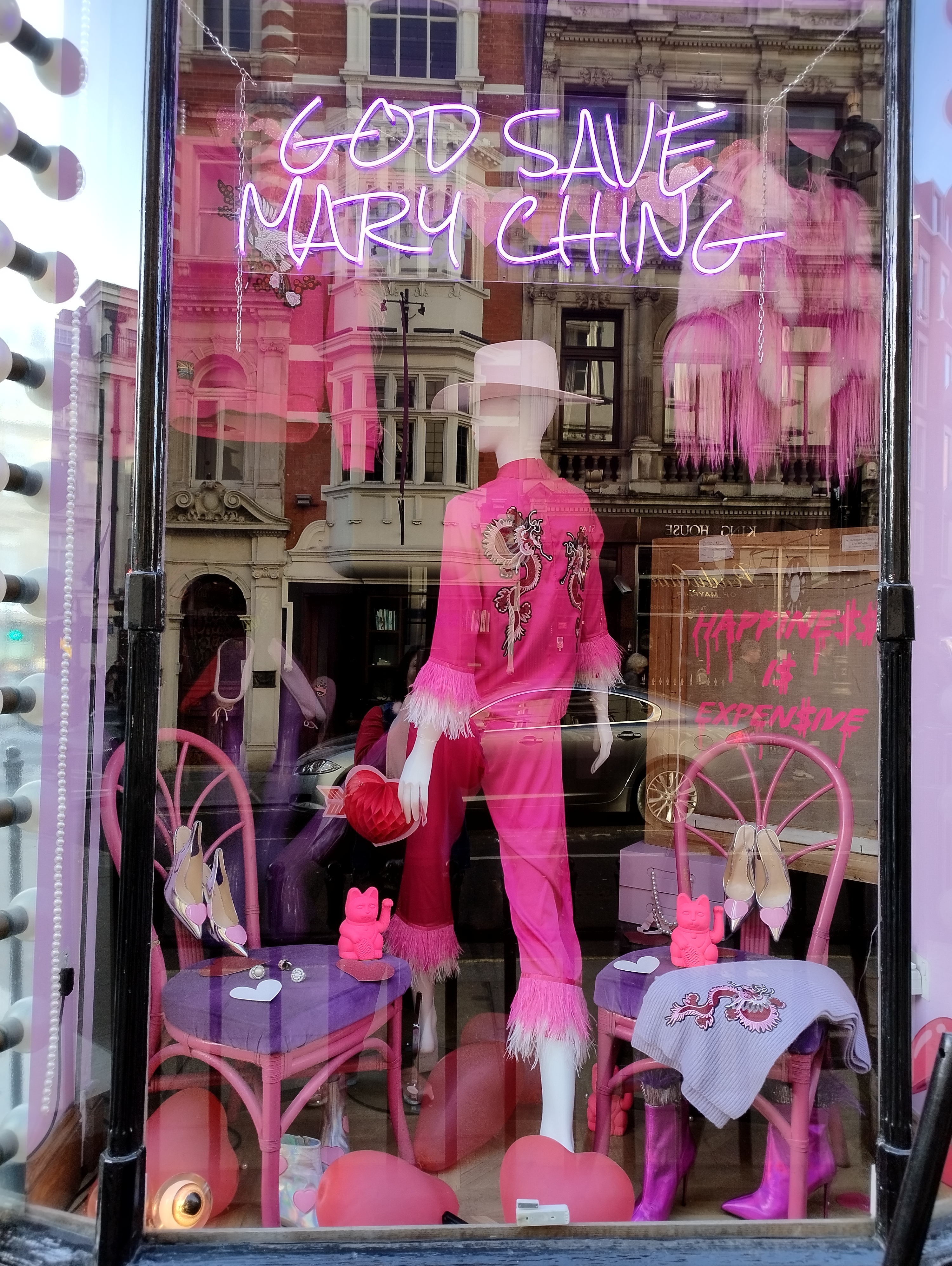 A store window display featuring a mannequin dressed in a vibrant pink outfit with fringe details.
