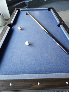A pool table with a blue felt surface featuring a pool cue resting diagonally across the table.