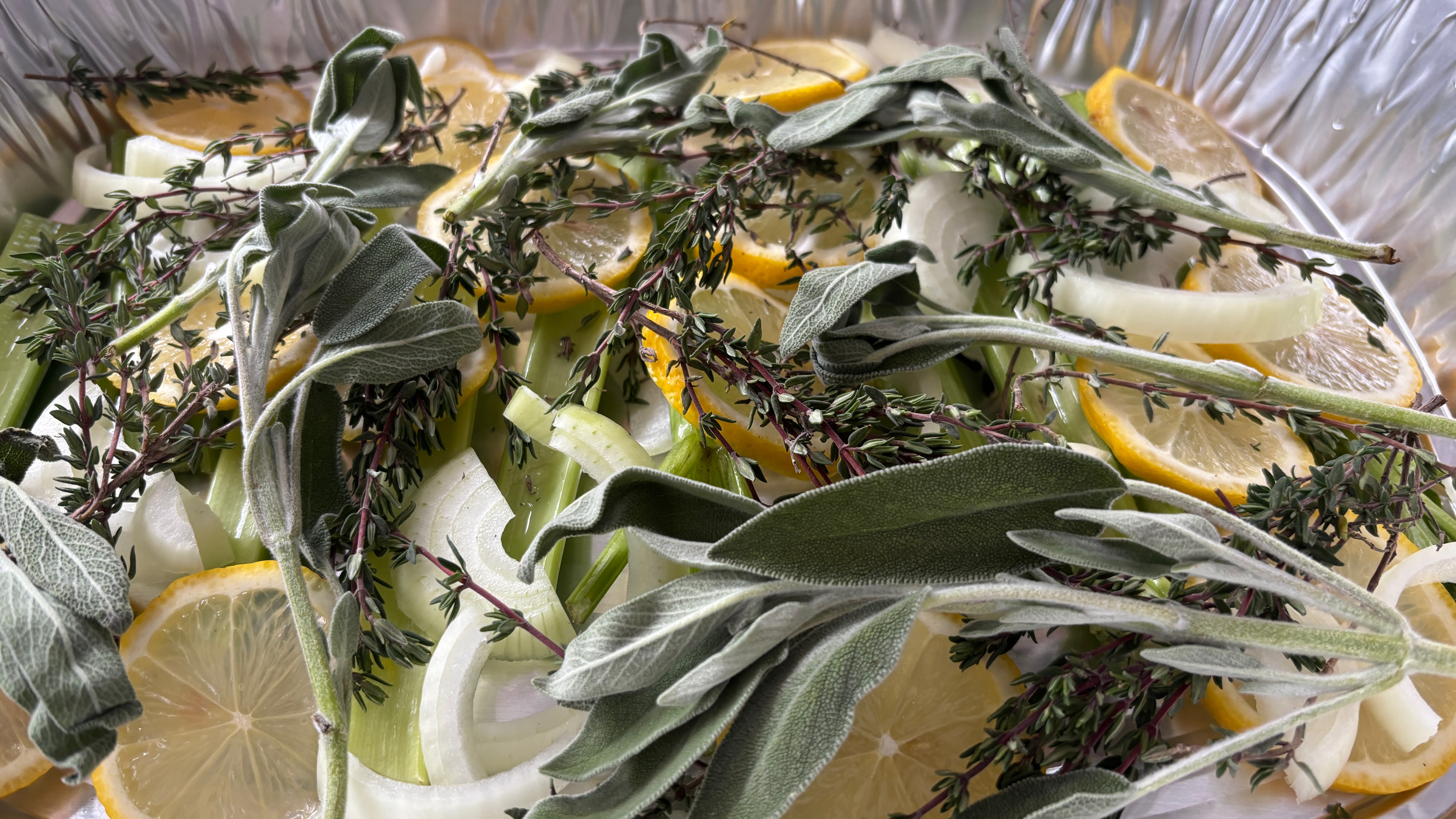 In a tin pan are sage, thyme, onions, lemon, and celery prepared as a base too cook a turkey on.