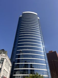 A tall, modern skyscraper with a curved glass facade and prominent horizontal stripes reflects the blue sky. 