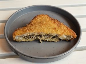 Chicken bread pocket (is a type of Japanese curry bread). It features a crispy, deep-fried exterior and a soft, flavorful curry filling inside. The curry appears to contain shredded chicken and spices, encased in a breaded and fried shell, served on a grey plate. Captured from a restaurant in Kozhikode, Kerala. 
