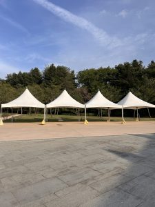 A row of white event tents with pointed tops is set up on a paved area.
