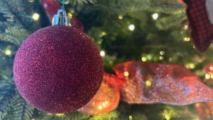 Closeup of a red ball ornament, covered in sparkles. Set in an evergreen tree.