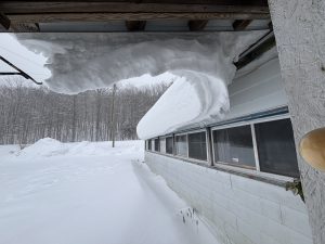 Snow curling off the roof of a home.